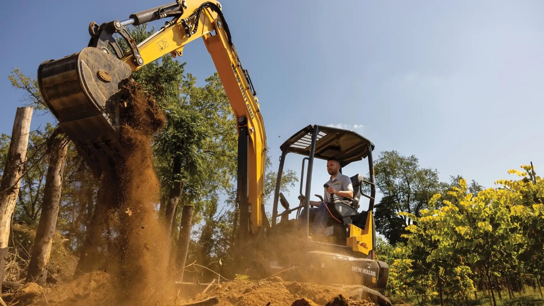 A tracked excavator working in dust and trees on a site