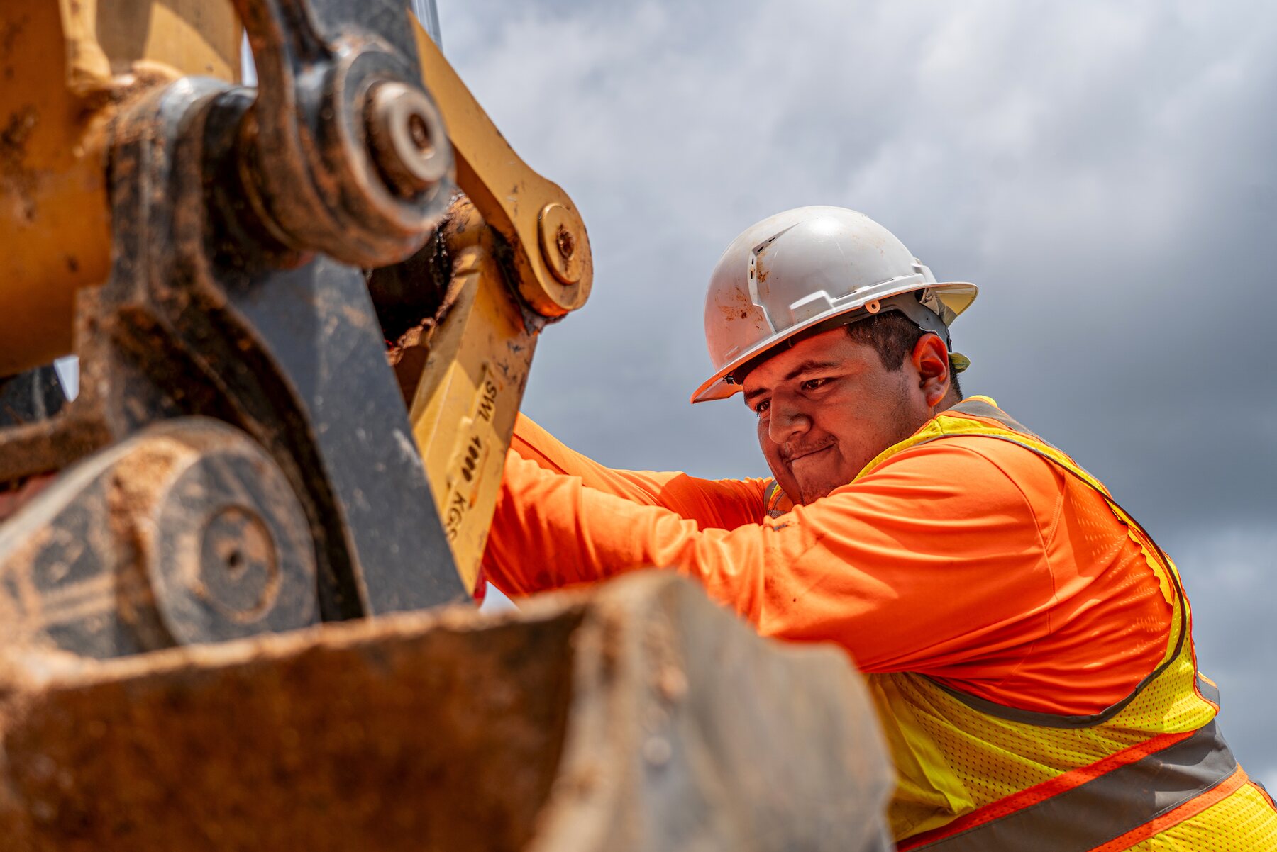 An operator in high-visibility clothing working at the bucket of an excavator