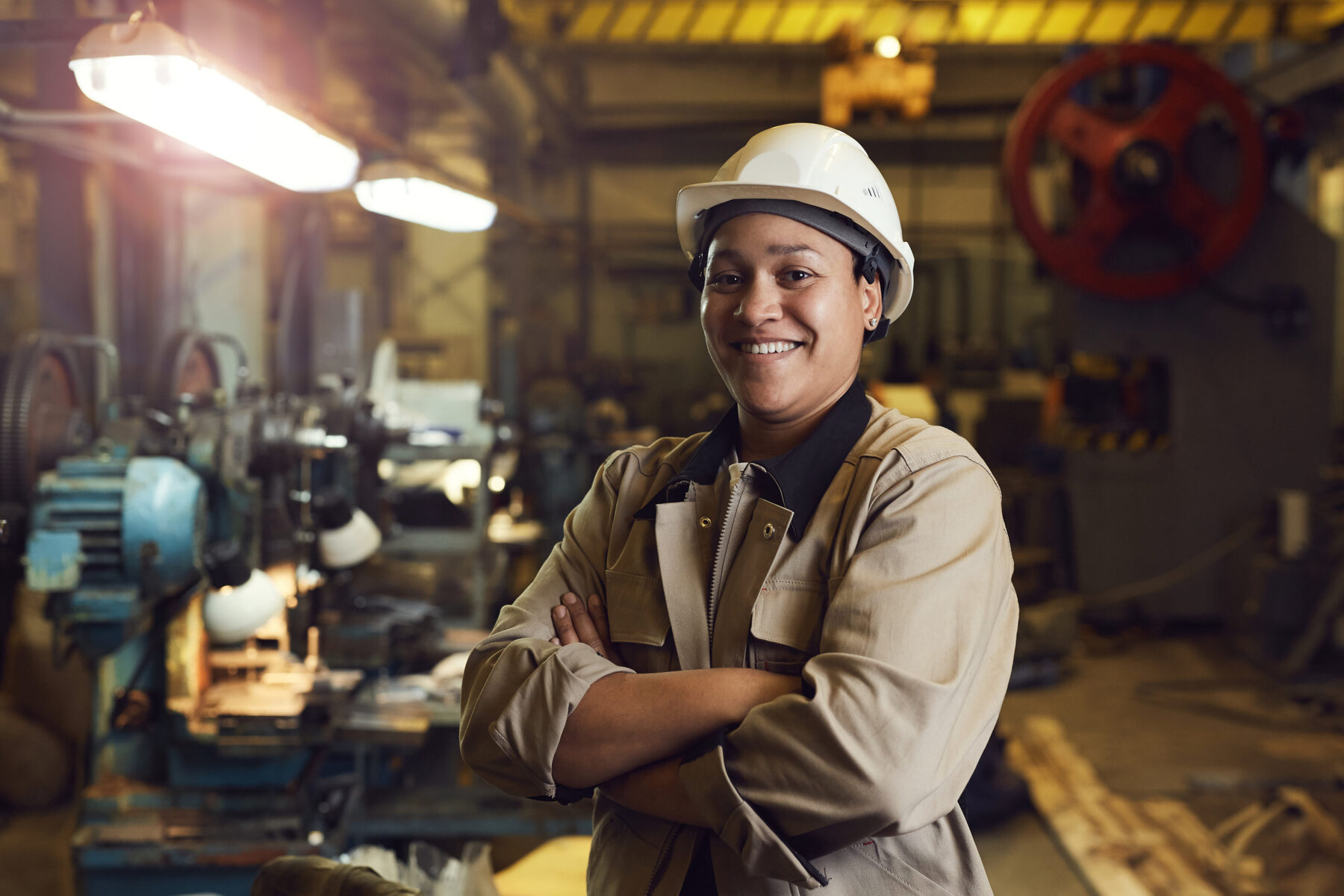 A tradesperson in a hard hat working at a bench in a fabrication shop