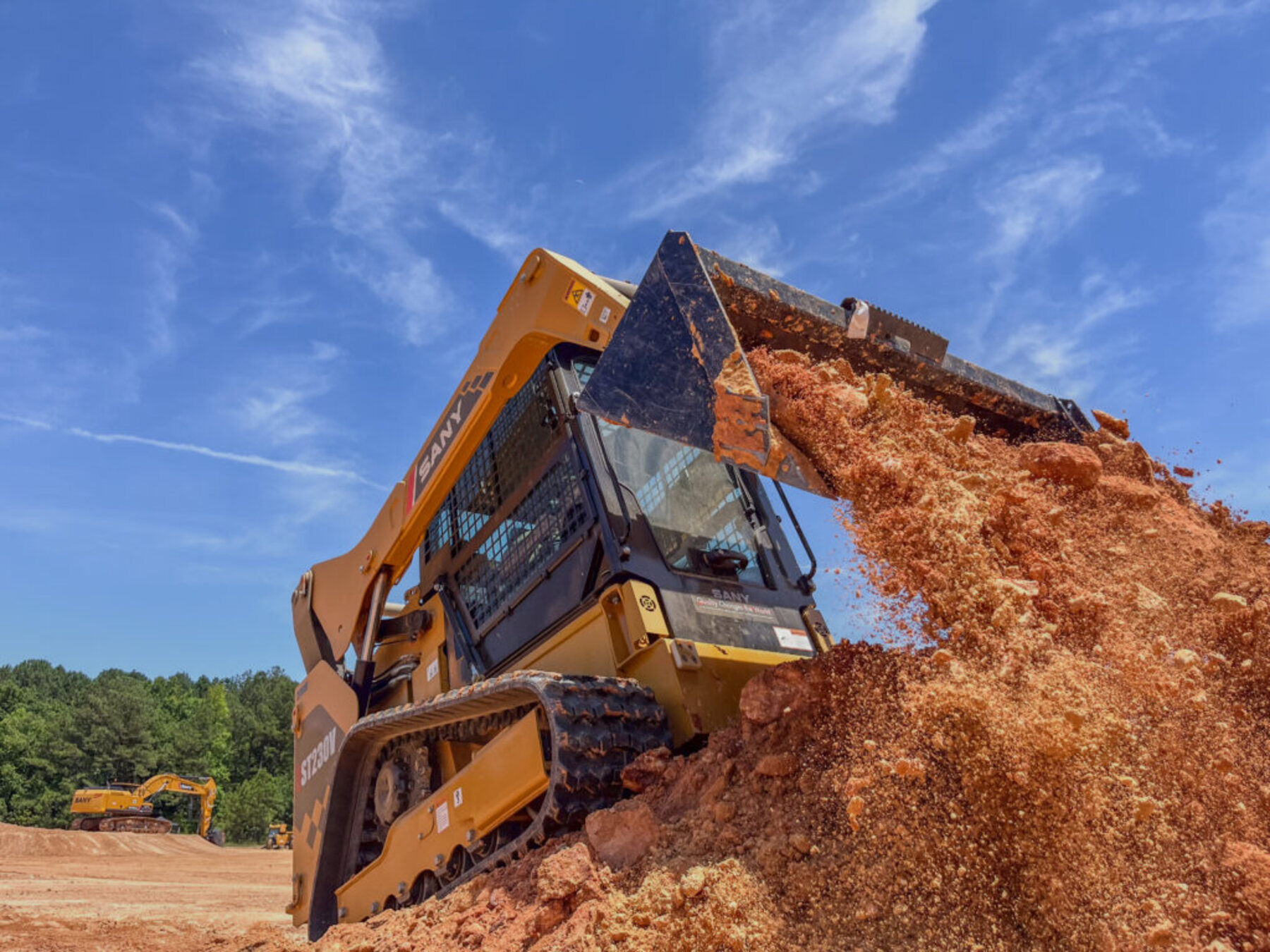 A tracked skid-steer loader tipping a bucket of material on a site